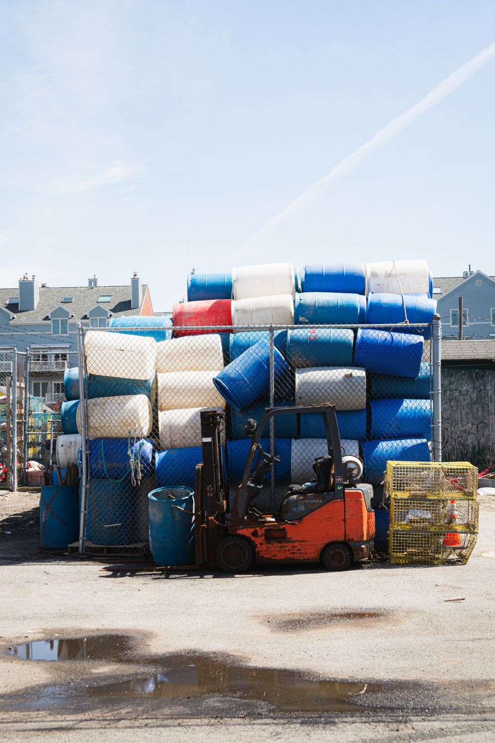 Stack of blue and white barrels loaded on an orange forklift in an industrial yard.