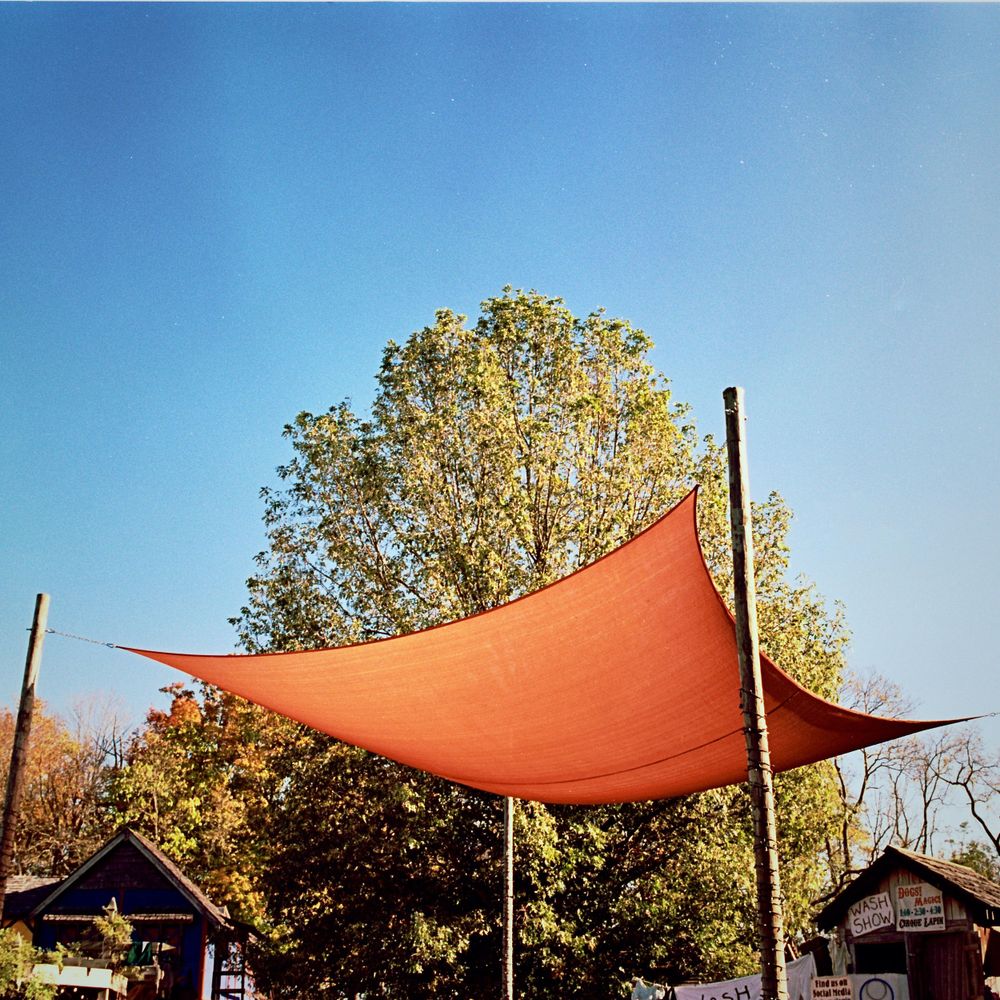 Large orange canvas canopy stretched between poles against a blue sky with autumn trees.