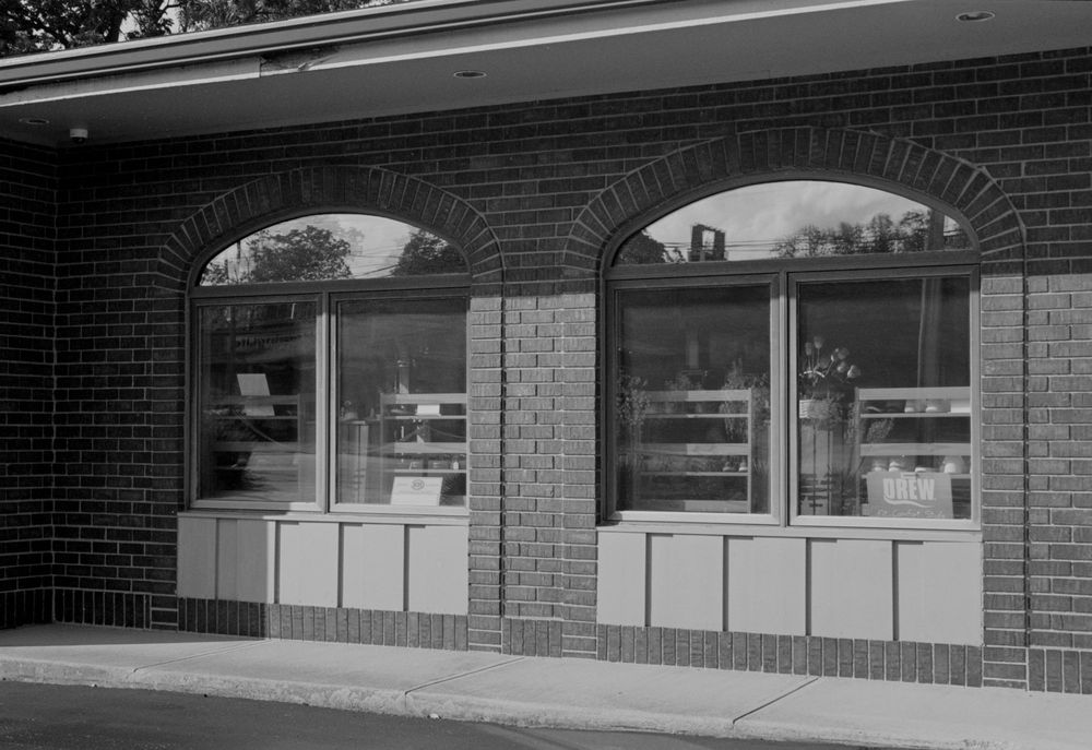 Black and white view of a vintage brick storefront with arched windows displaying retail displays behind glass panels.