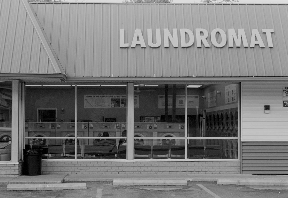 Black and white exterior view of storefront signage for a laundromat business on a commercial building facade.