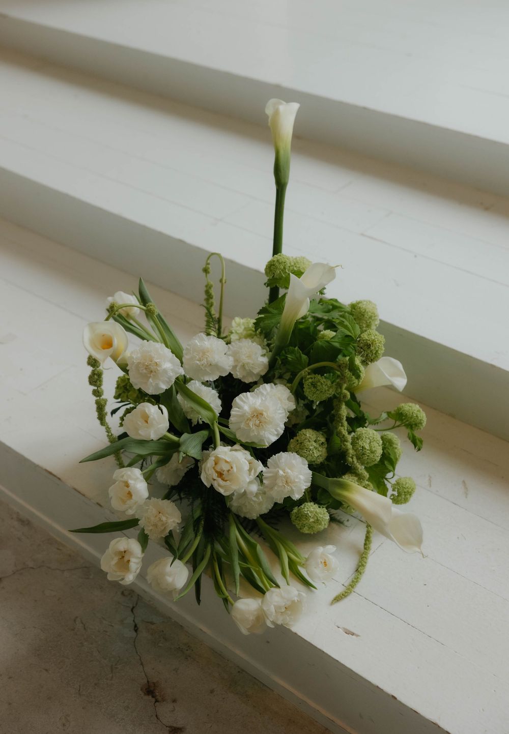 Elegant bridal bouquet of white calla lilies, roses, and green blooms resting on white staircase steps.
