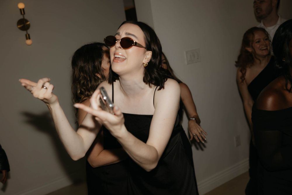Guest in black dress and sunglasses dancing enthusiastically at a lively wedding reception party.