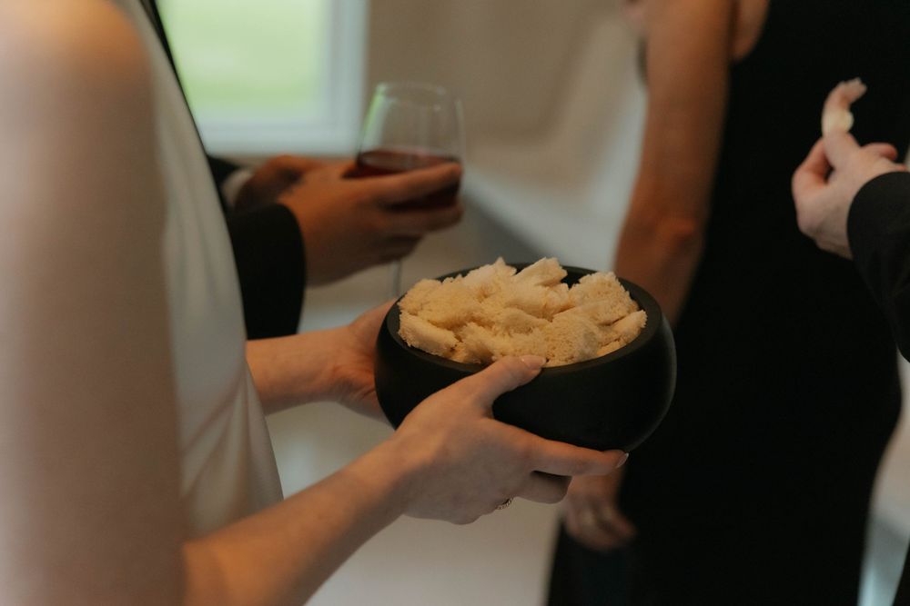 Person holding black bowl of white cheese snacks at elegant gathering with wine glass visible.