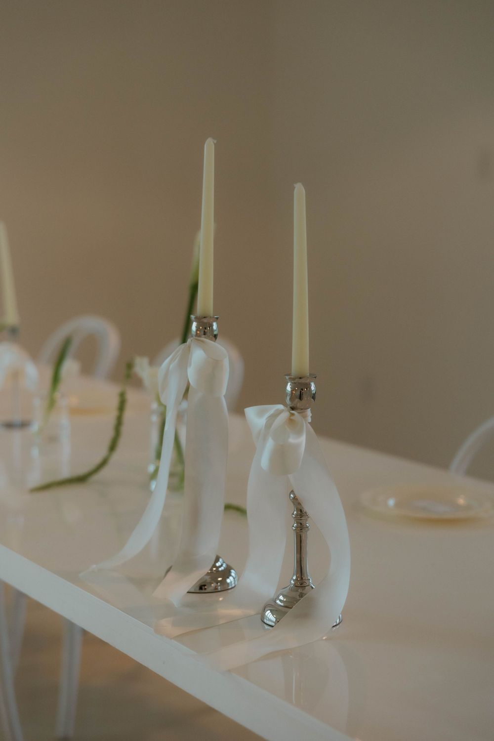 Elegant white wedding unity candles with silver holders and ribbon bows on a white table.