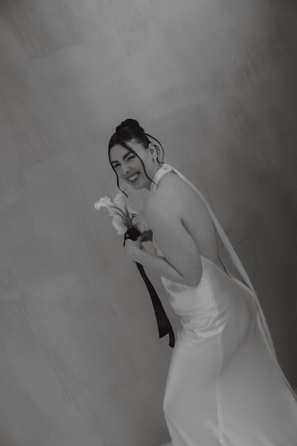 Black and white photo of a laughing bride in a white halter gown holding white flowers.