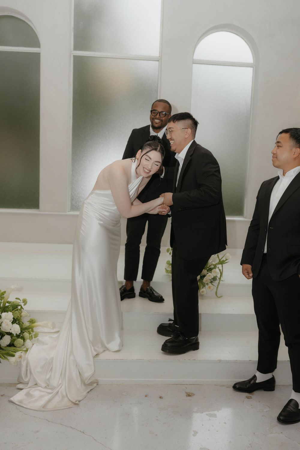 A bride in a white gown shares a joyful moment with the groom and guests at the altar.