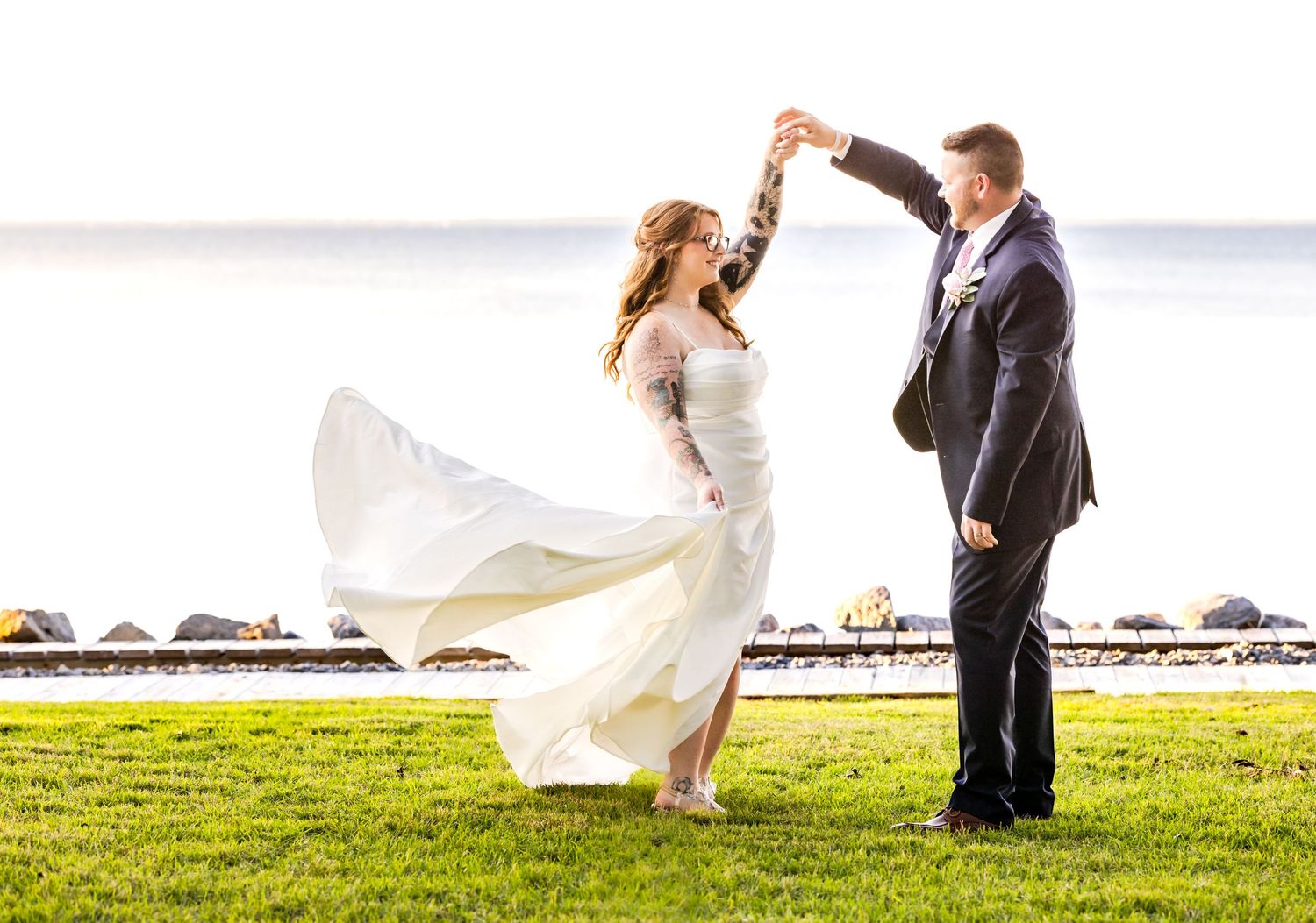 Couple dancing together on a grassy waterfront during their wedding celebration.