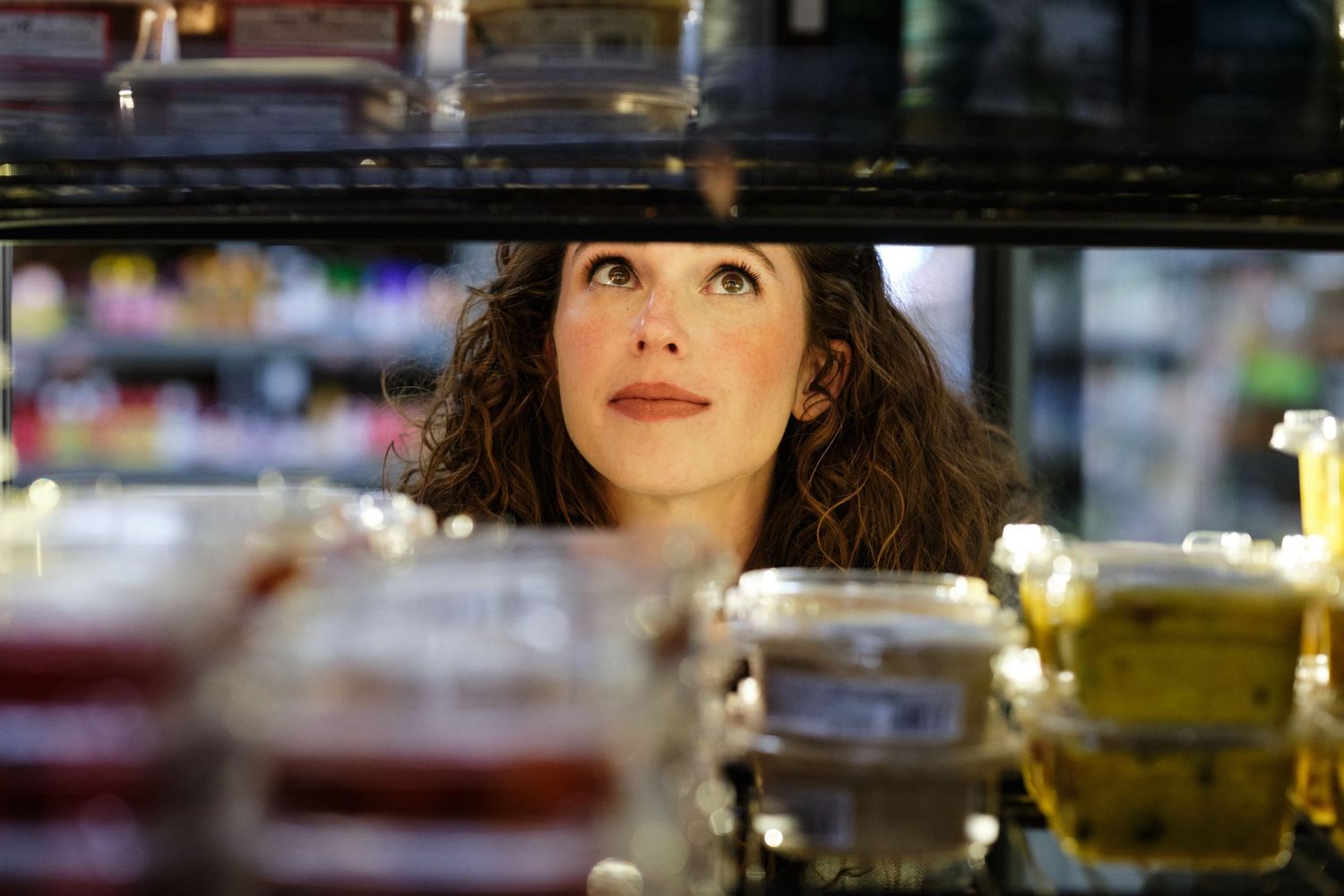 Looking up through glass jars and containers at a backlit shelf in a bar or restaurant setting.