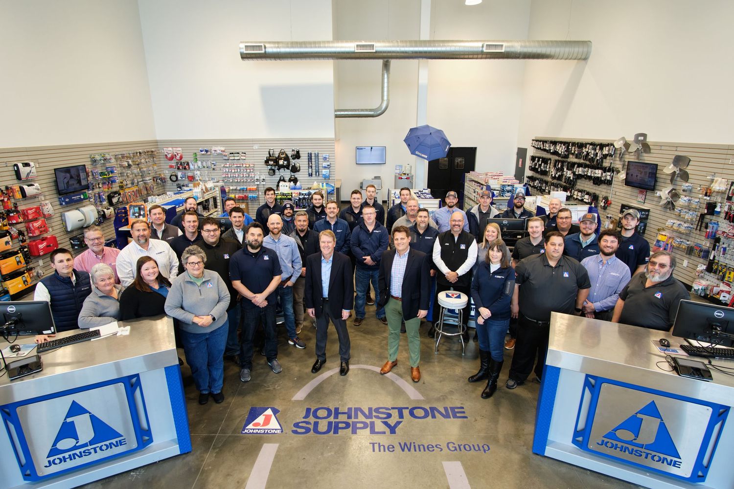 Large group of employees gathered in an industrial workplace setting with banners and display materials visible on the walls.