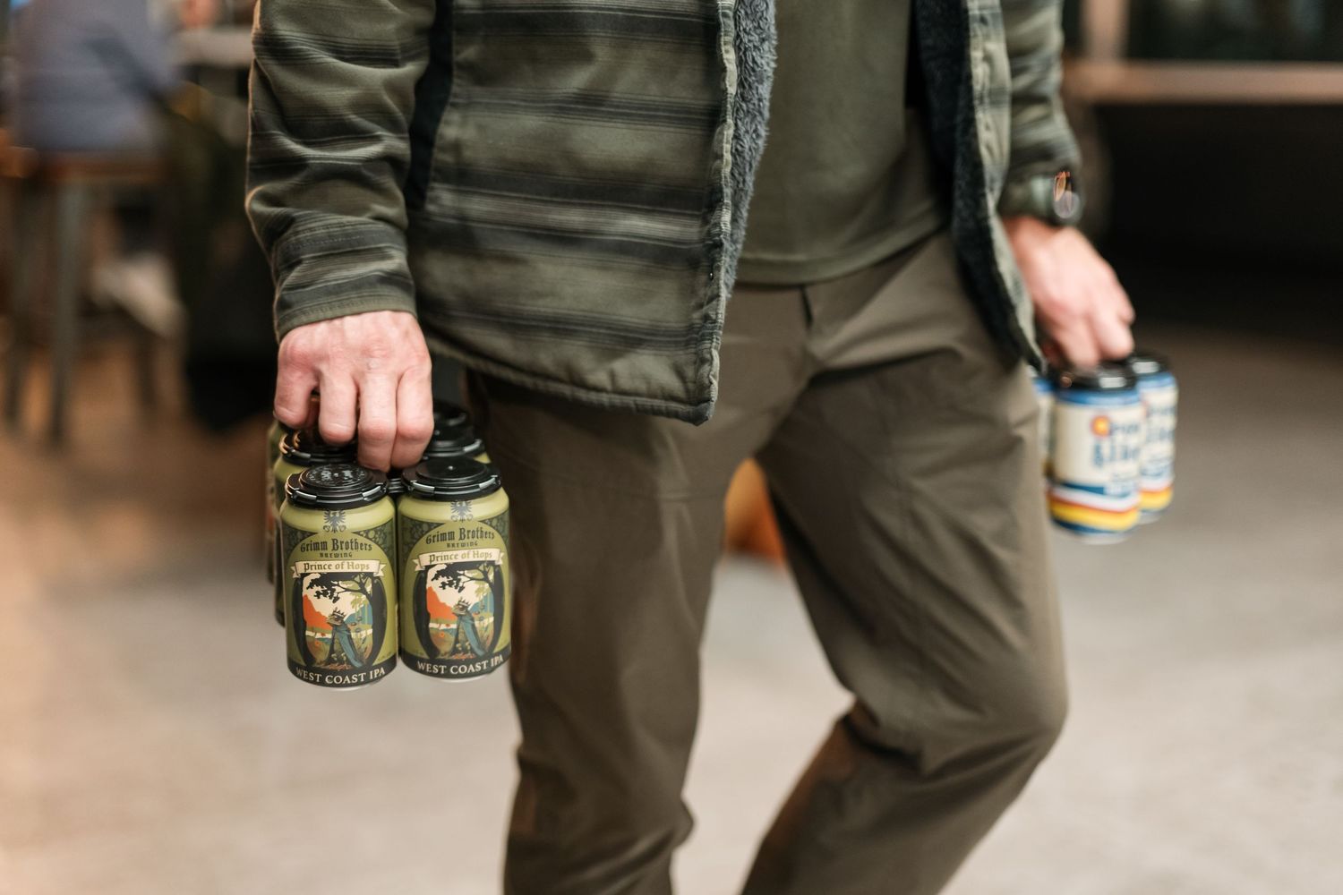 Person wearing olive green pants holds several glass jars of pickles or preserves while walking.