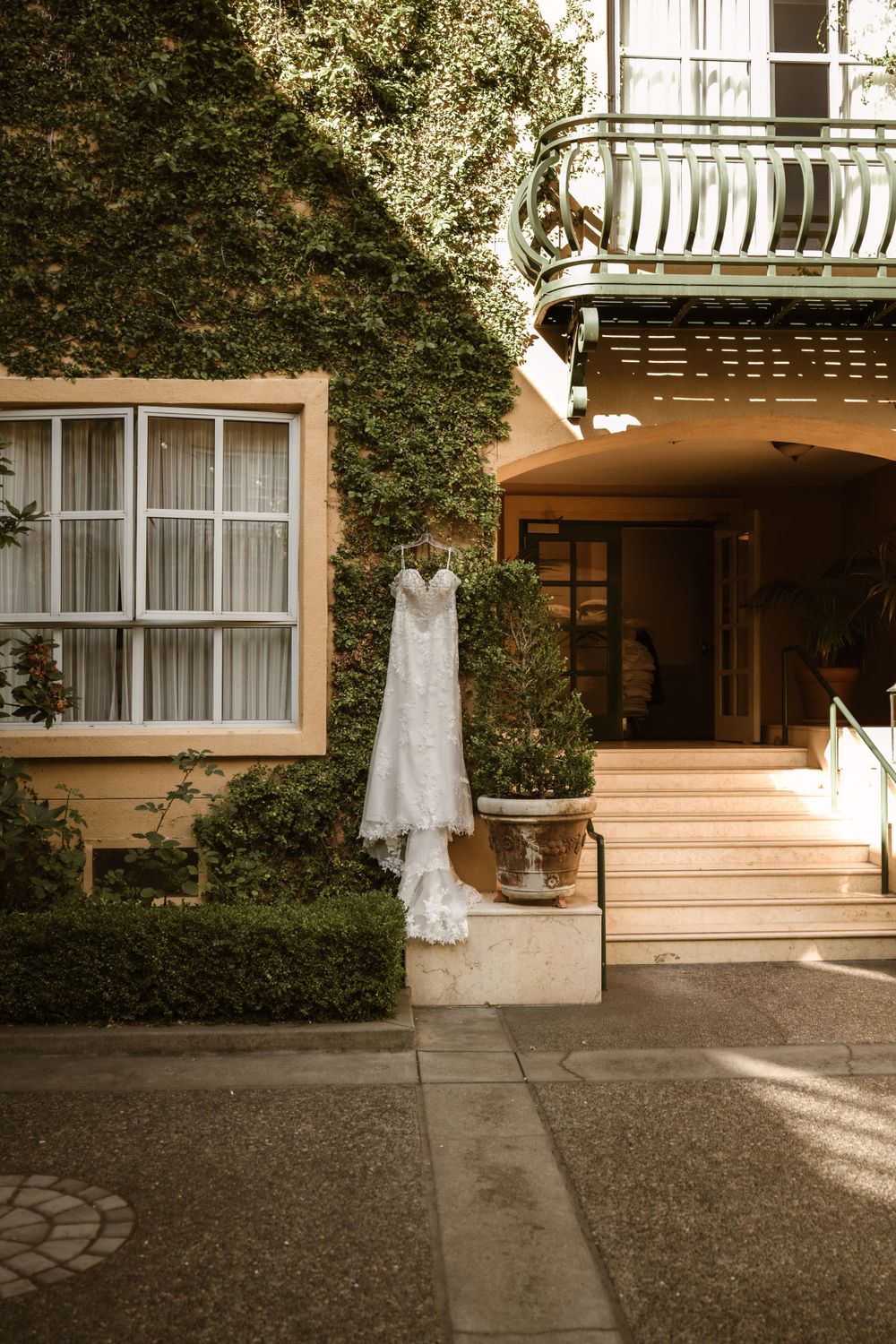 Wedding dress displayed in sunlit garden setting with architectural elements.