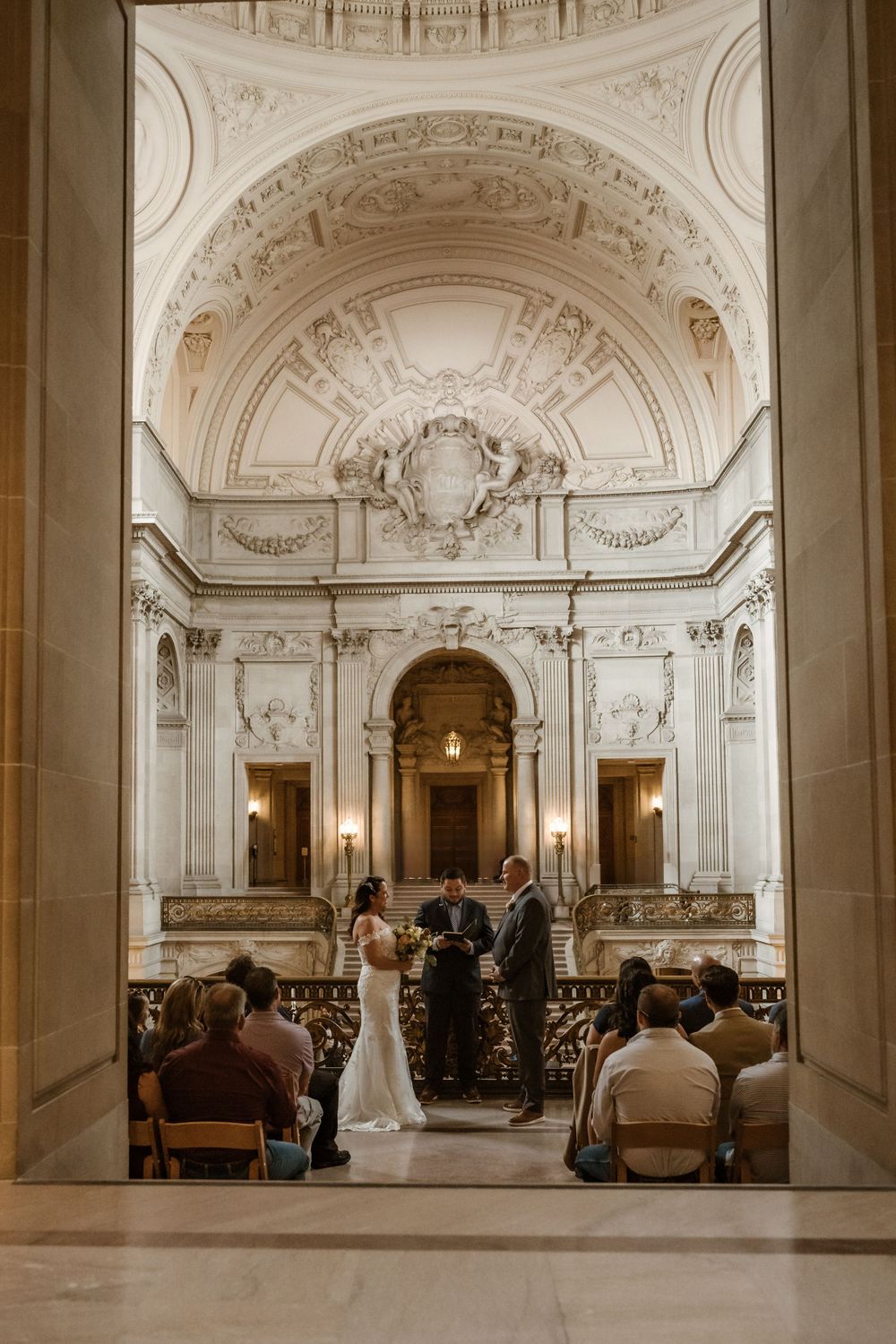 Wedding ceremony taking place in elegant marble hall with ornate architectural details.