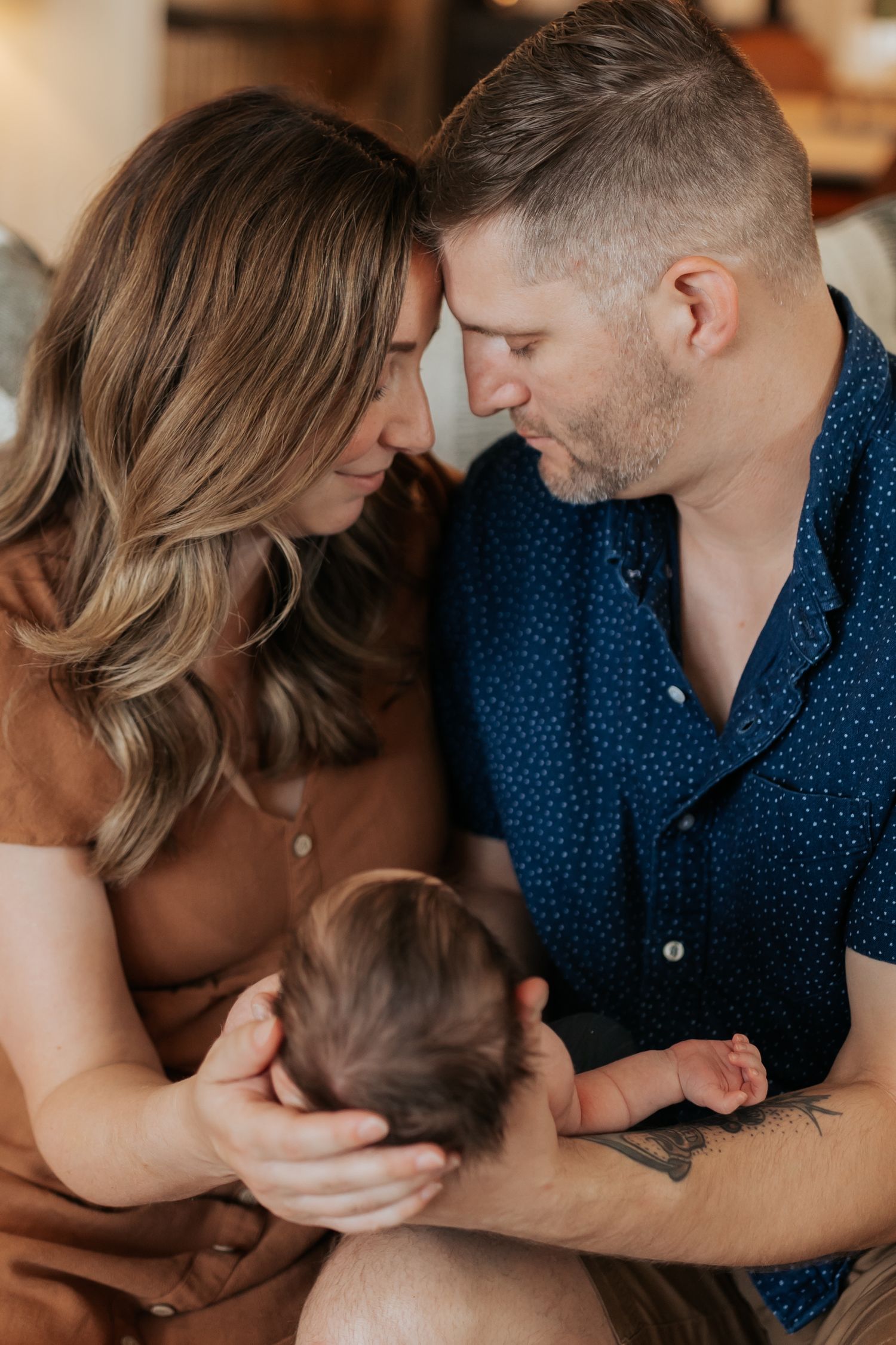 a couple sitting close to each other and leaning foreheads together, while holding a baby in their arms