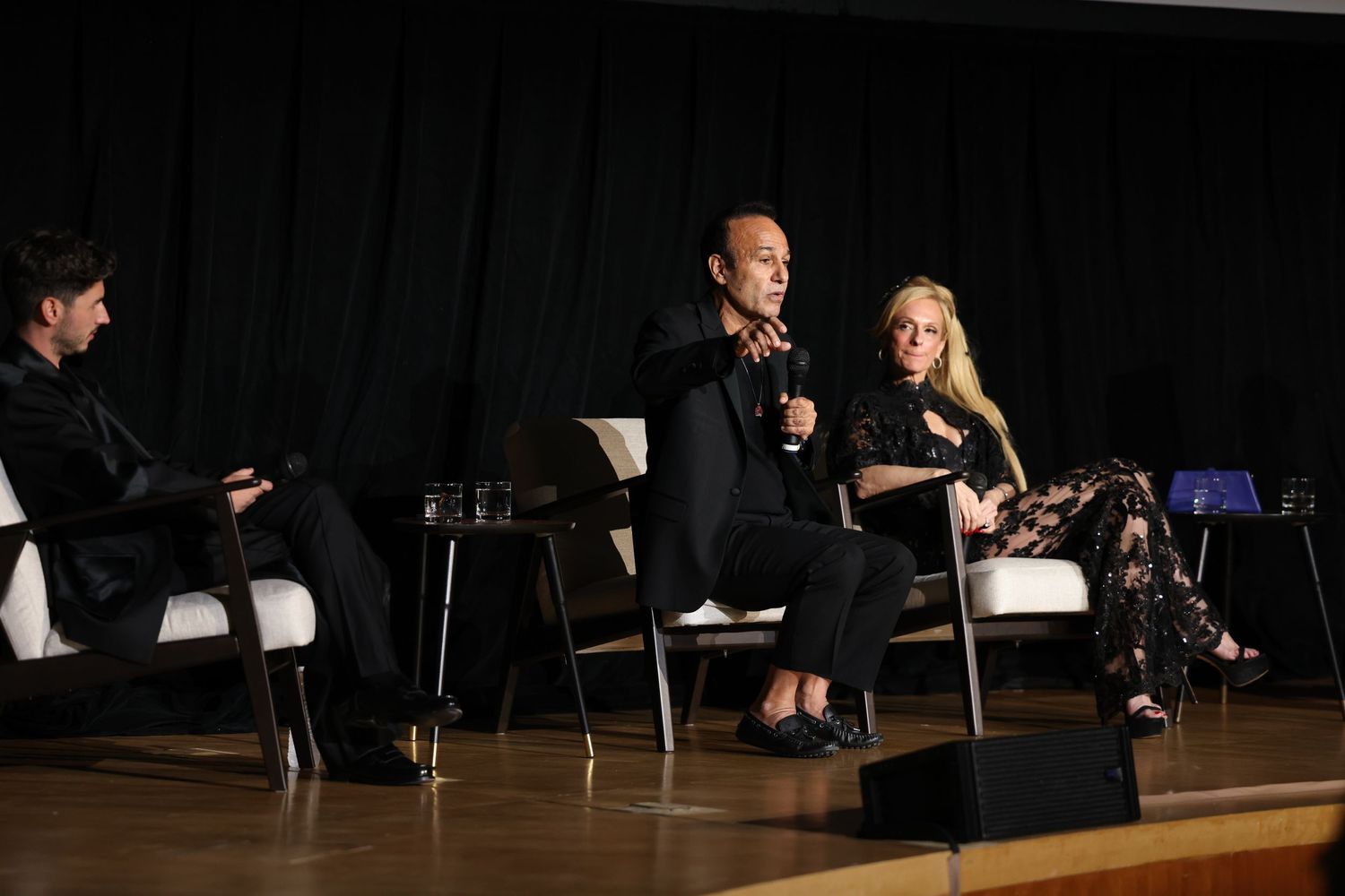 A panel discussion takes place on stage with three people seated in chairs during a presentation.
