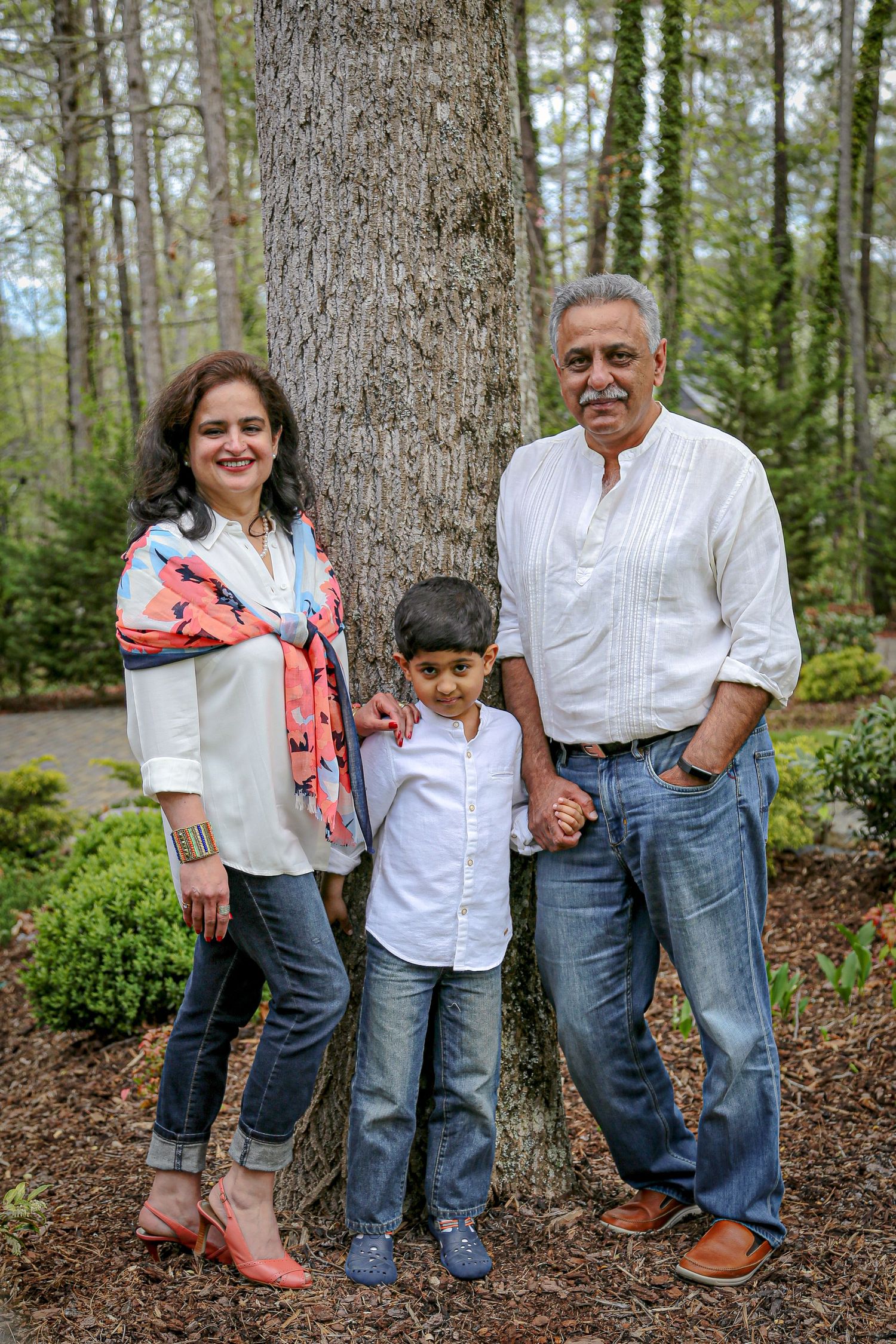 Three people stand together in front of a large tree trunk in a lush forest setting.