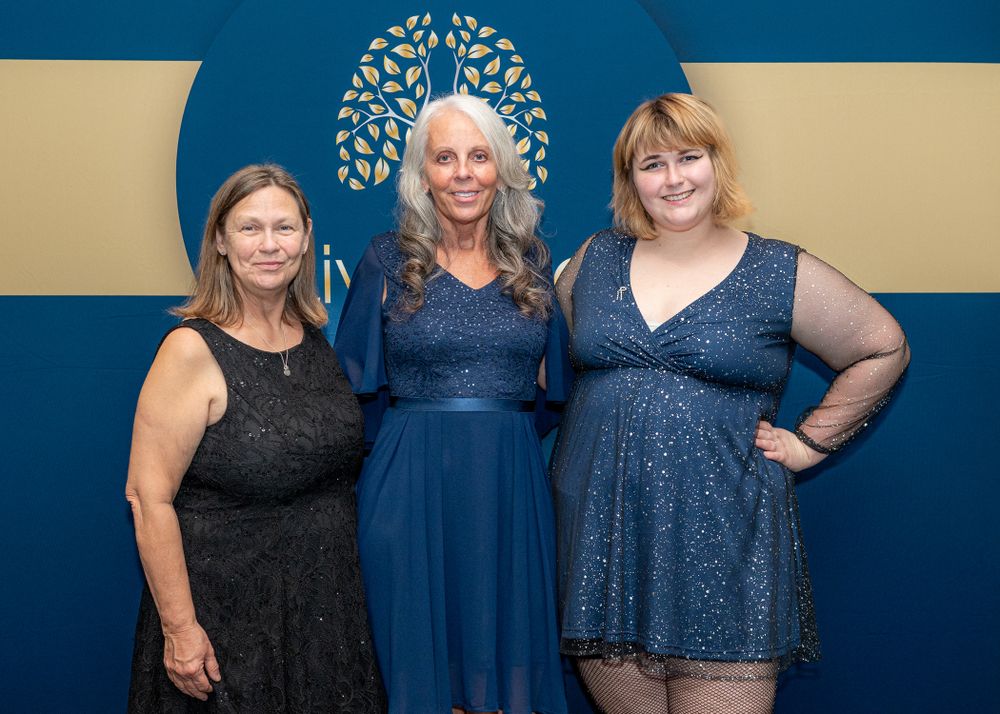 A group wearing navy blue dresses poses together against a dark blue background for a formal event.