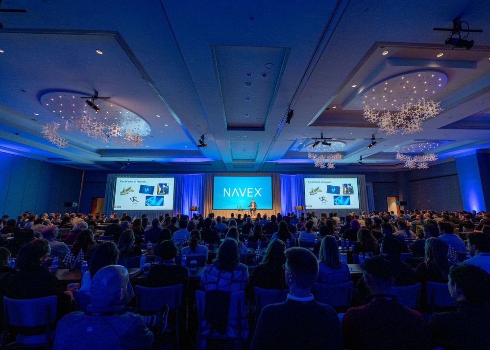 Large conference room filled with attendees under blue lighting for a professional presentation.
