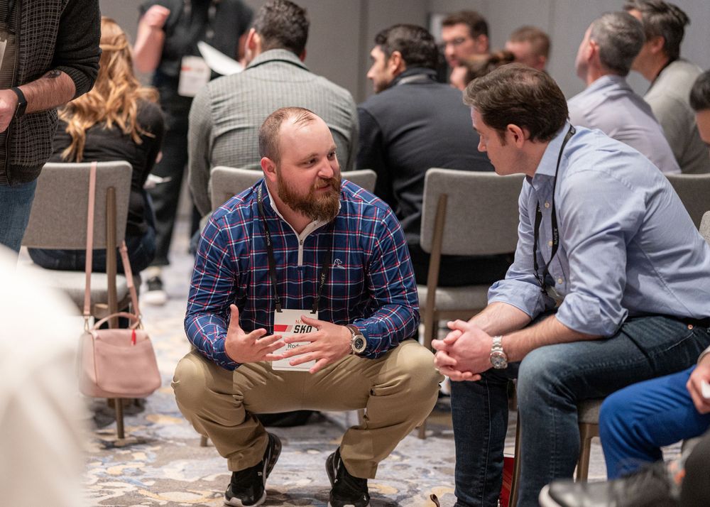 Two people having casual conversation while seated at indoor event.