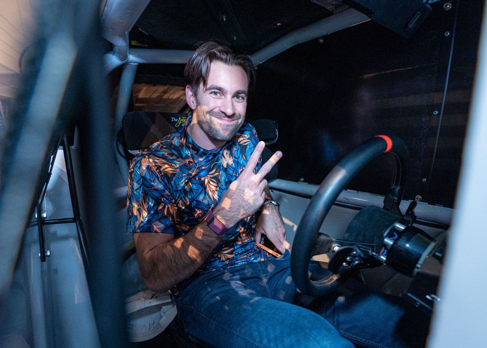 Person in floral shirt shows peace sign while seated in vehicle.