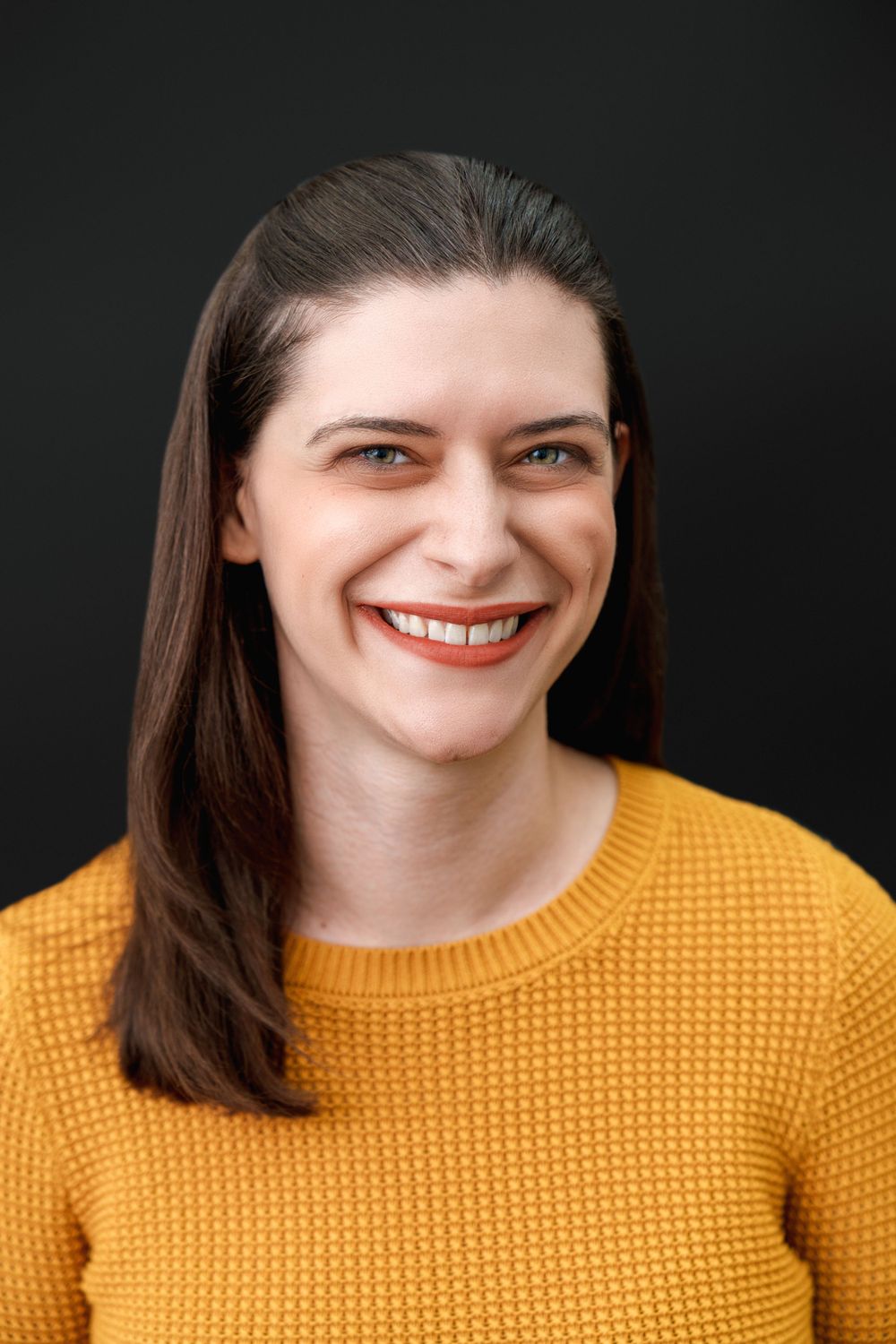 Professional headshot against black background wearing yellow knit sweater.