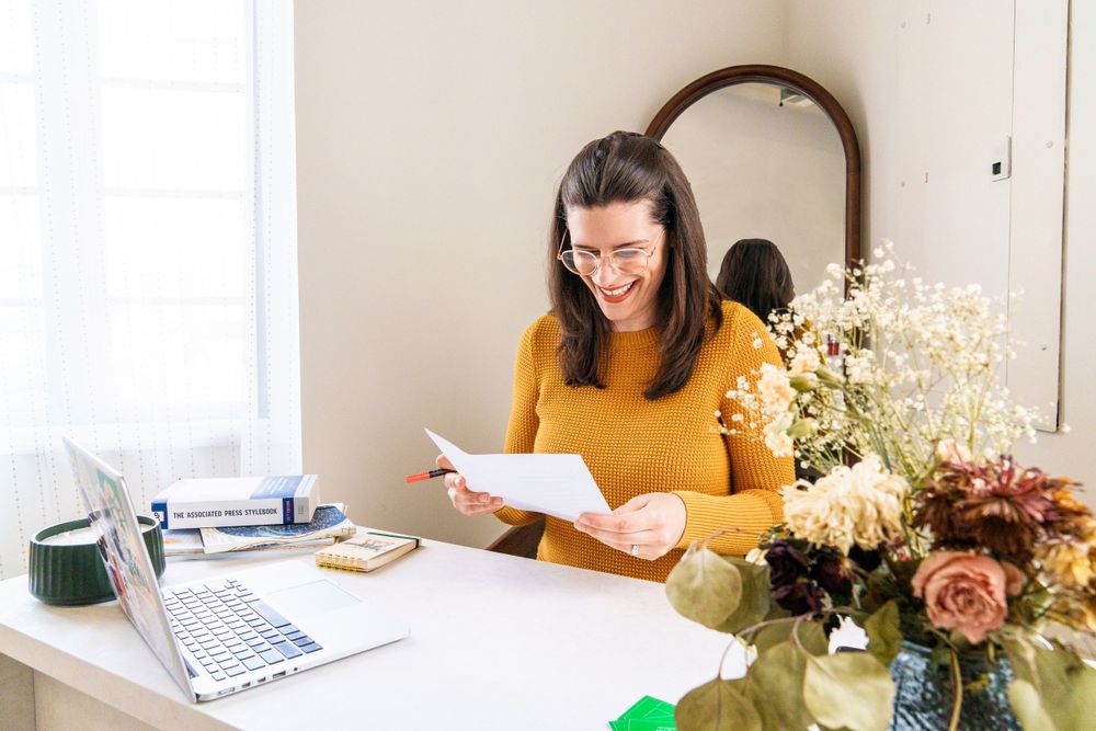 Student studying at desk with laptop and floral arrangement.