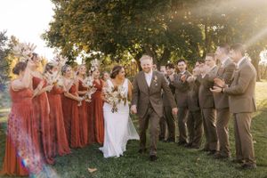 Wedding party in burgundy dresses and grey suits celebrating outdoors during golden hour.