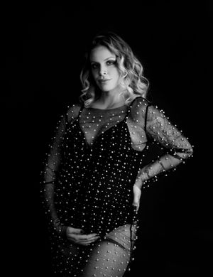 Maternity portrait in sparkly black dress against dark background.