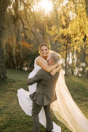 Romantic wedding moment with couple embracing under autumn willow trees at sunset.