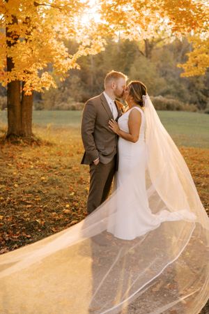 Fall wedding portrait with golden leaves and flowing veil during sunset.