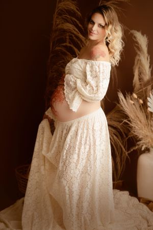 Maternity photo in vintage-style lace dress with pampas grass backdrop.