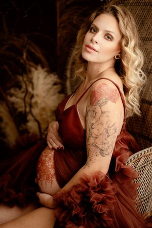 Romantic maternity boudoir photo in burgundy dress with rustic decor.