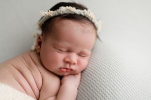 Close-up of sleeping newborn with delicate floral crown on textured gray background.