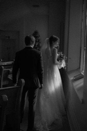 Black and white photo of bride and groom standing in church by window.