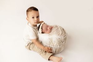 Siblings sharing sweet moment as older child holds wrapped newborn on white background.