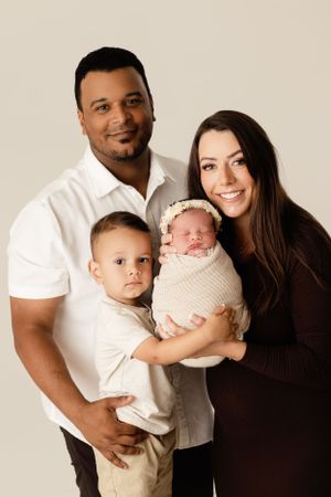 Family portrait with interracial couple holding their two children against neutral background.
