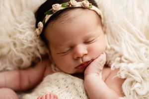 Sleeping newborn baby wearing floral headband on white textured blanket.