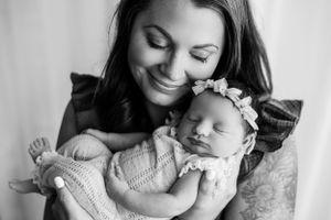 Peaceful newborn baby sleeping against parent in black and white portrait.