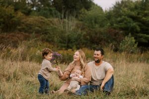 A family sits together in a sunny meadow during golden hour surrounded by tall grass.