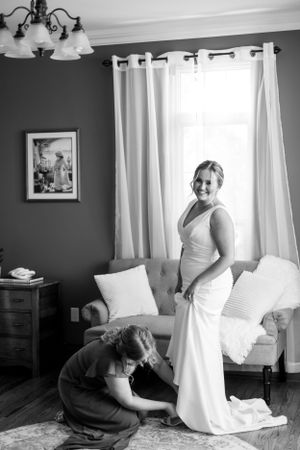 Black and white photo of wedding preparation in a sunlit room with white curtains.