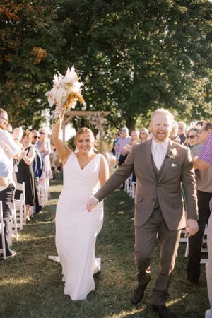 Wedding recessional with couple walking down aisle while guests celebrate outdoors.