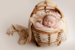 Sleeping newborn nestled in woven basket with cream-colored wrapping.
