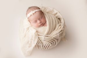 Peaceful sleeping newborn wrapped in textured cream fabric against light background.