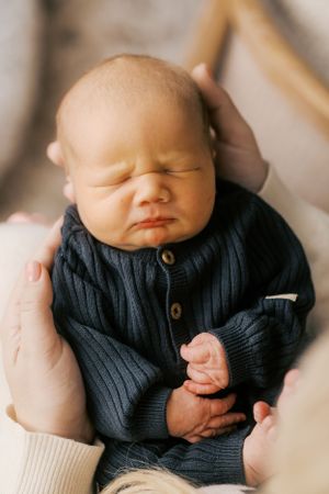 Sleeping newborn baby wearing navy blue knit sweater cradled in gentle hands.
