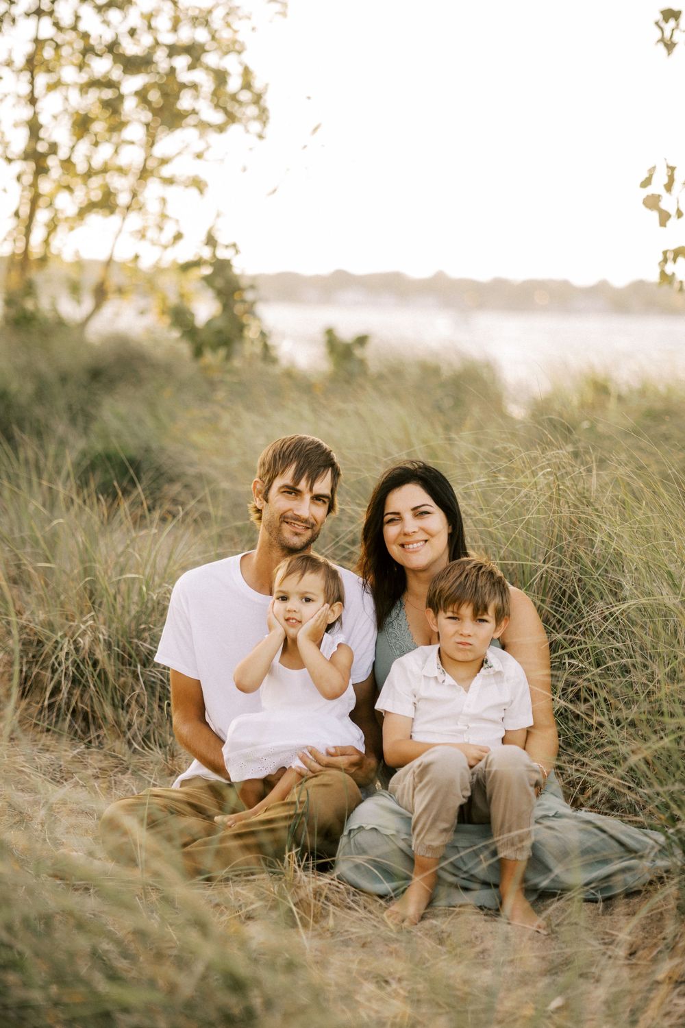 Family sits together on hillside during golden sunset surrounded by tall grass.