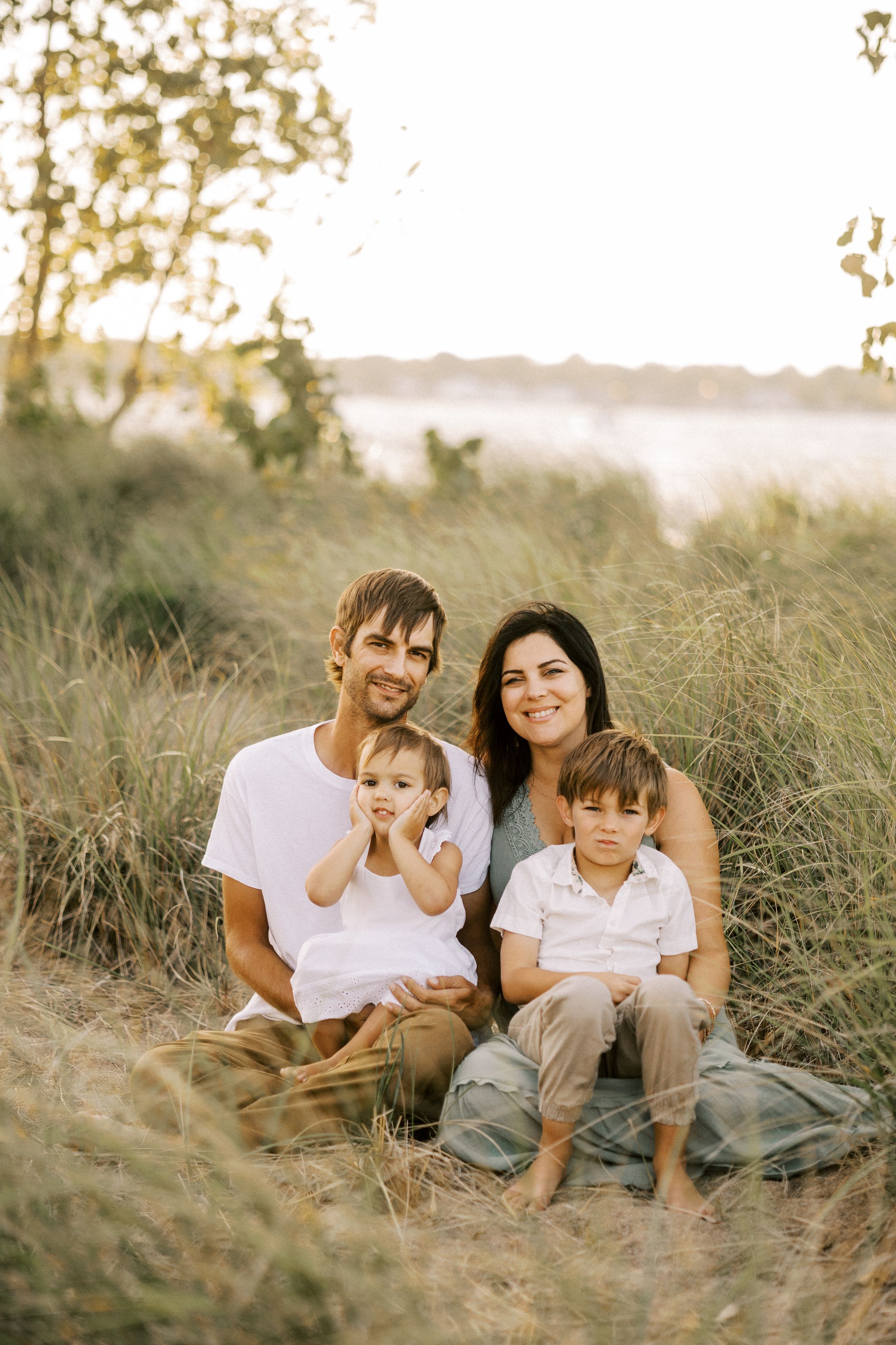 Family sits together on hillside during golden sunset surrounded by tall grass.