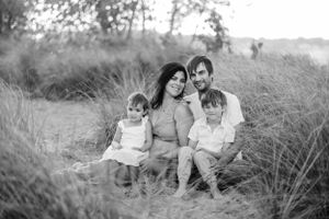 Black and white portrait of family sitting together in rustic outdoor setting.