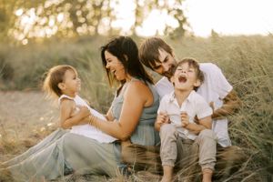 Family shares joyful laughs together while sitting in field at sunset.