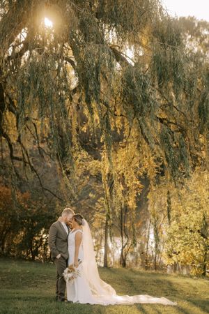 Romantic sunset wedding photo under golden willow trees beside a lake.