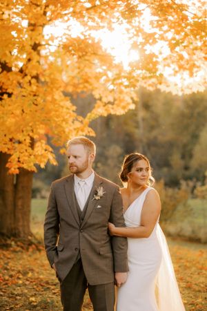 Autumn wedding portrait with vibrant orange maple leaves and golden sunlight.
