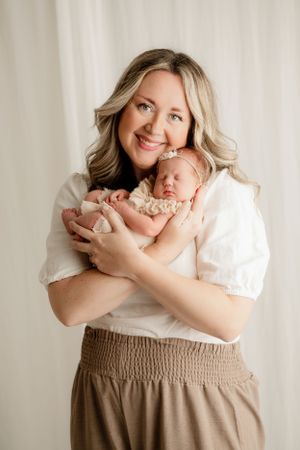 A tender portrait of mother holding sleeping newborn against white backdrop.